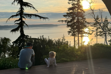 Parent and child sitting together at sunset with a backdrop of trees and water on Camano Island