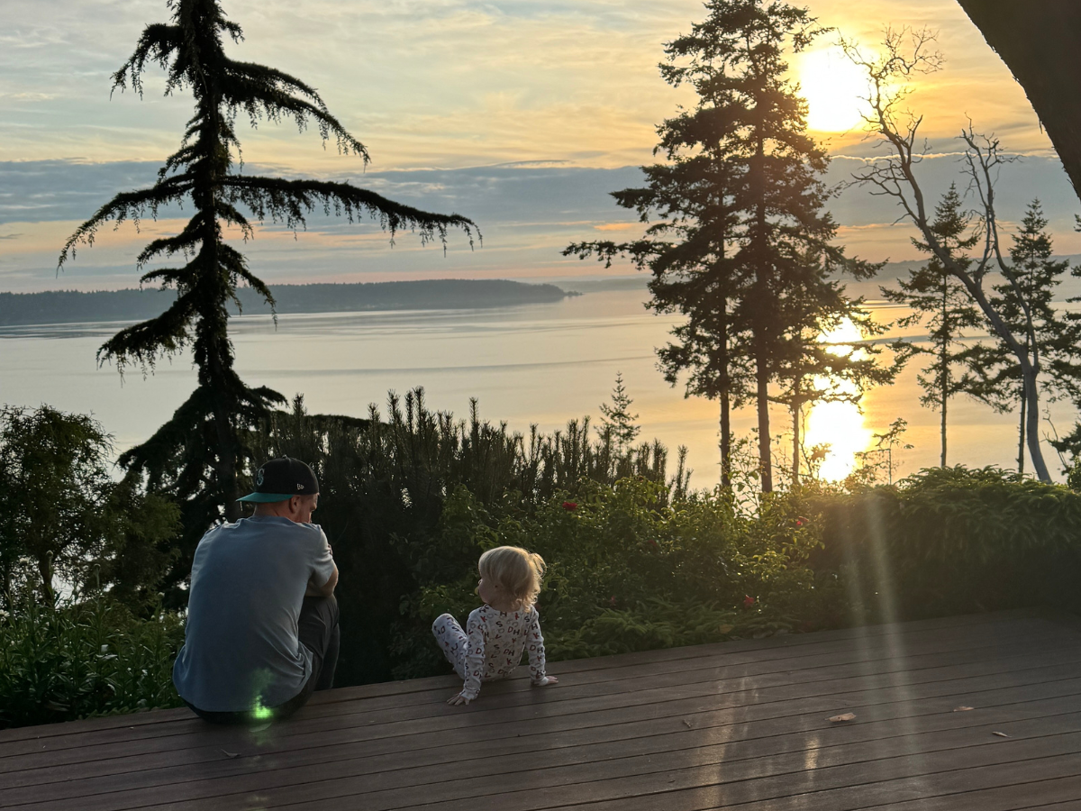Parent and child sitting together at sunset with a backdrop of trees and water on Camano Island