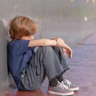 Student sits slumped against school hallway wall, looking down