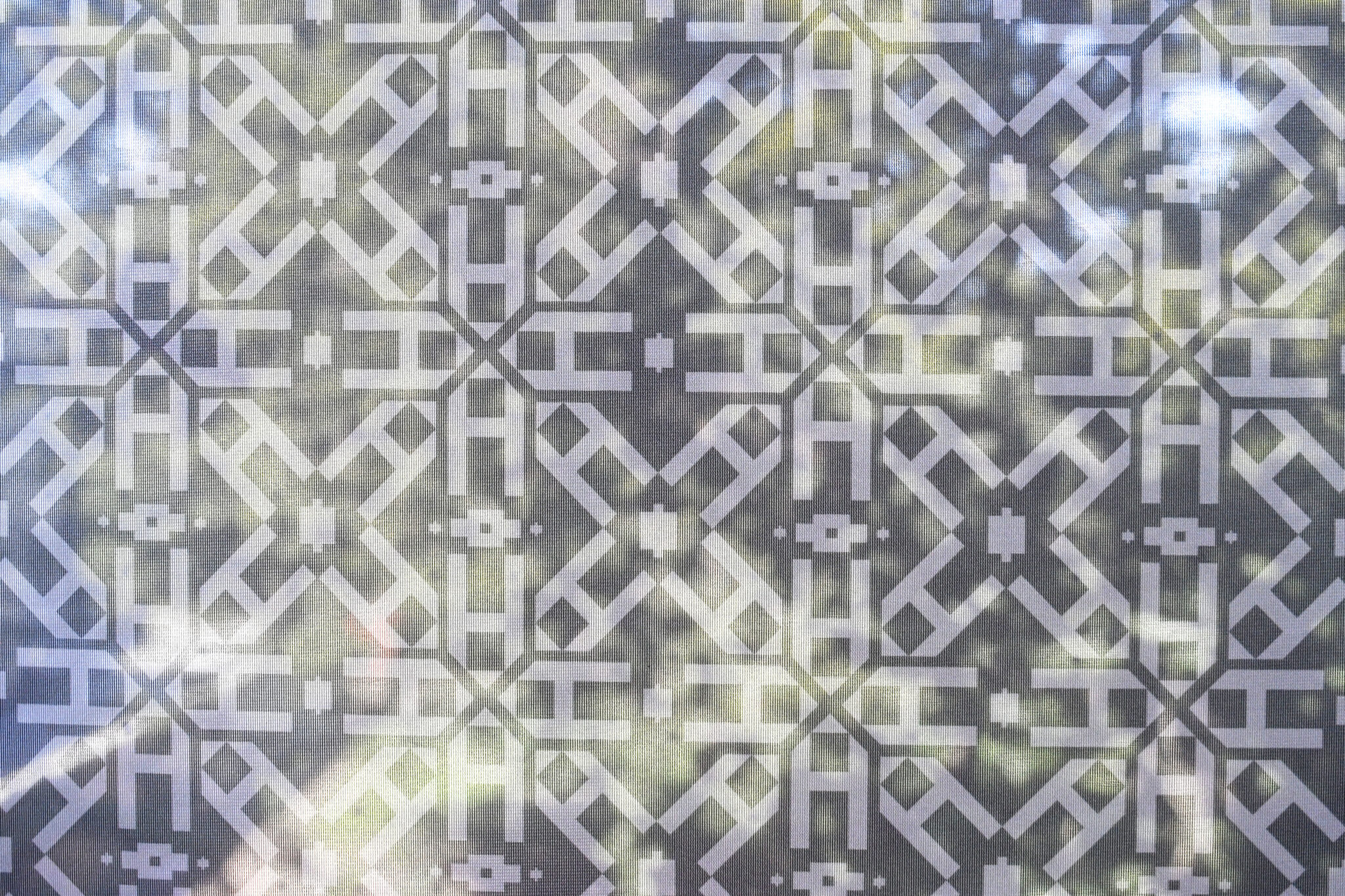Closeup of the patterned scrim at the Geometry of Light exhibit, featuring repeating A’s.