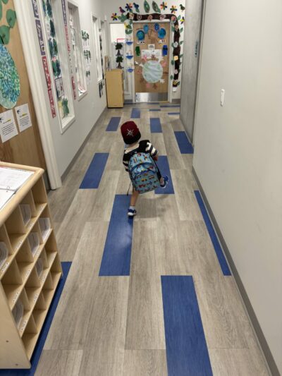 Preschooler skipping on colorful floor tiles down the school hallway.