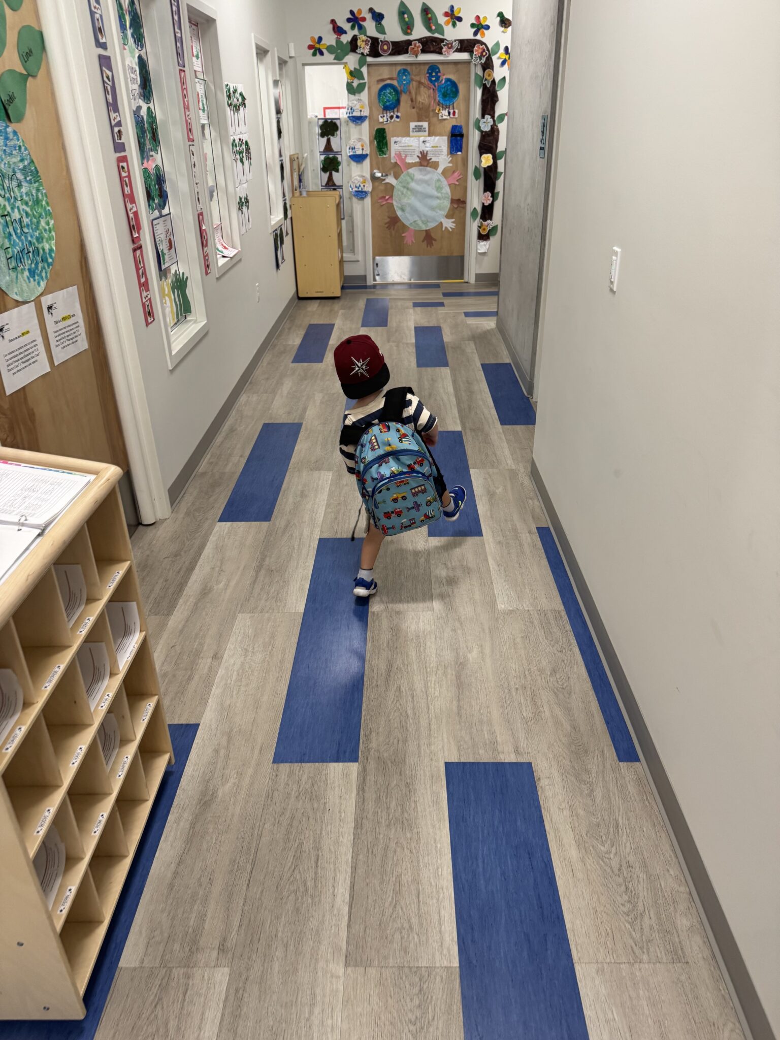 Preschooler skipping on colorful floor tiles down the school hallway.