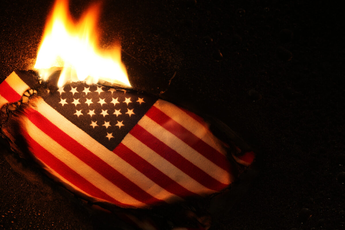 An American flag set on fire during a protest, symbolizing dissent and debate over free speech rights.