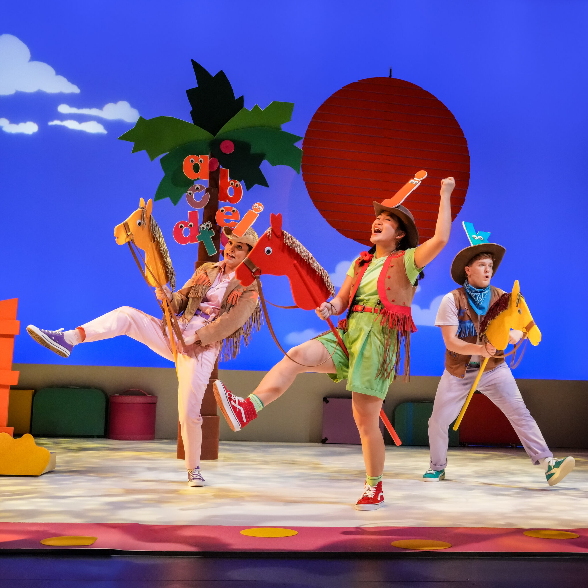 Three actors dressed as letters perform a lively rodeo scene with hobby horses in Chicka Chicka Boom Boom: The Musical at Seattle Children’s Theatre.