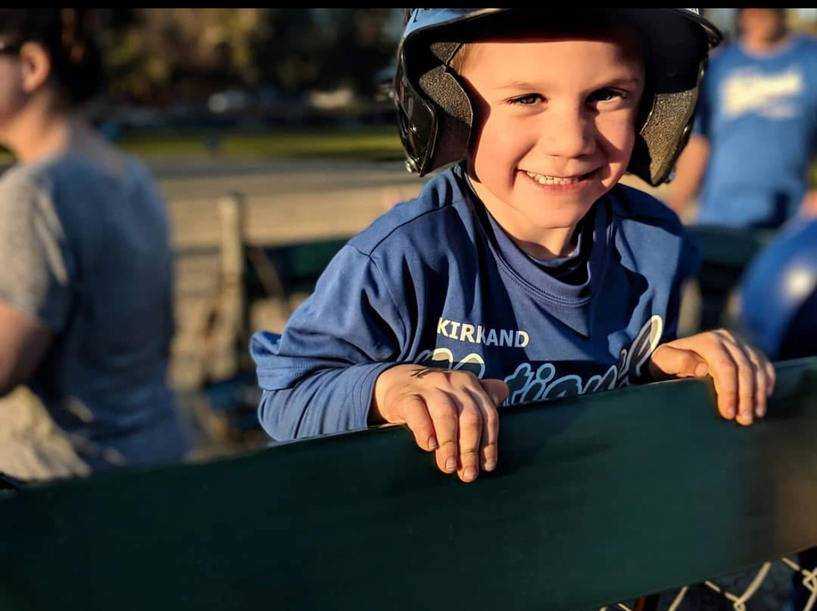 Young child smiling in a baseball uniform before a game.