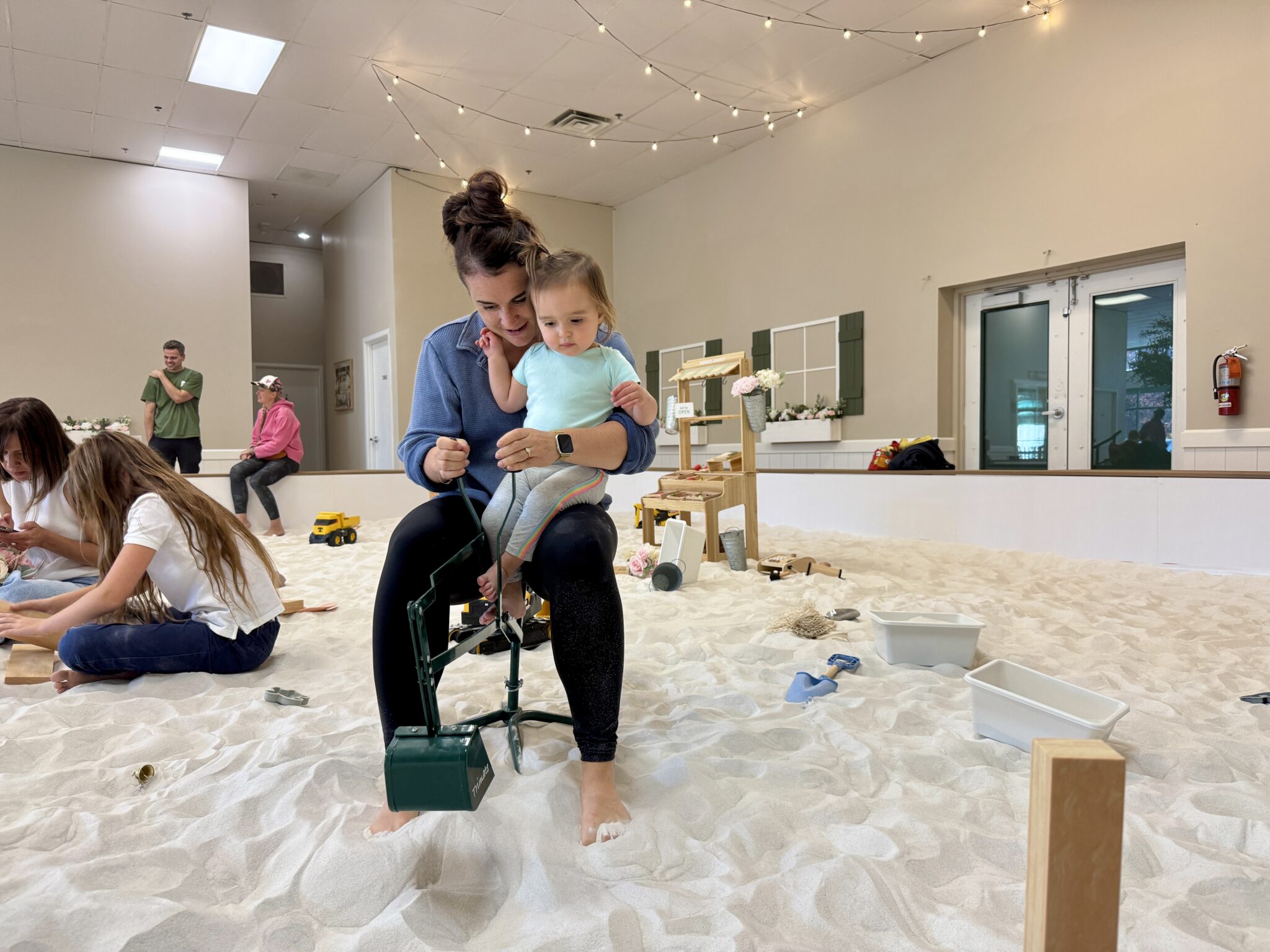 Mother and toddler sitting together on a toy digger inside SandGarden’s indoor sandbox in Issaquah