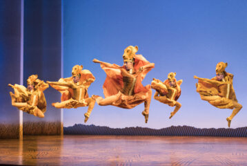 Actors in elaborate costumes perform “The Lion King” on stage.