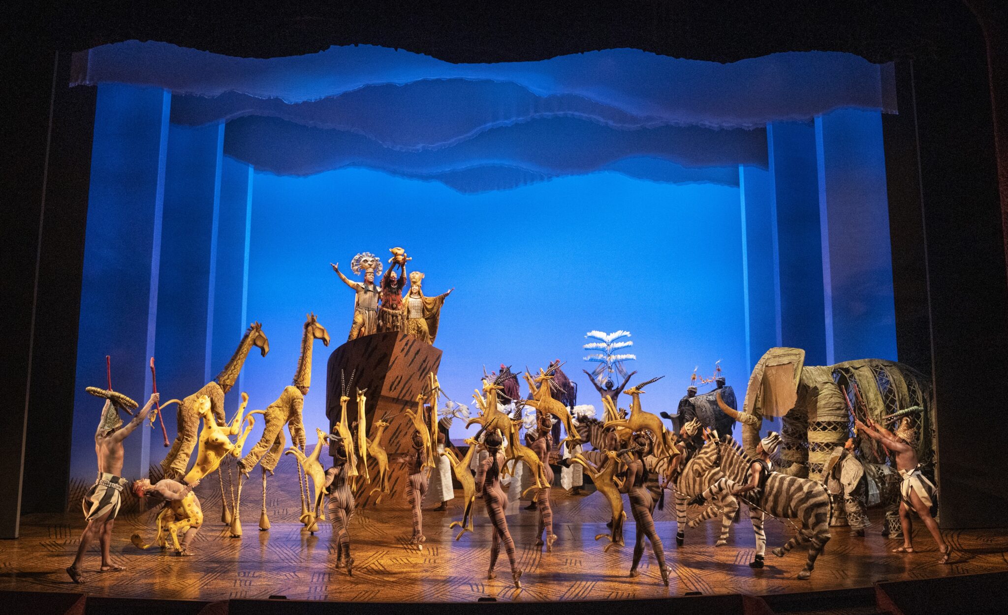 Actors in elaborate costumes perform “The Lion King” on stage.
