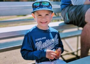 Kid in full baseball uniform smiling proudly at the camera.