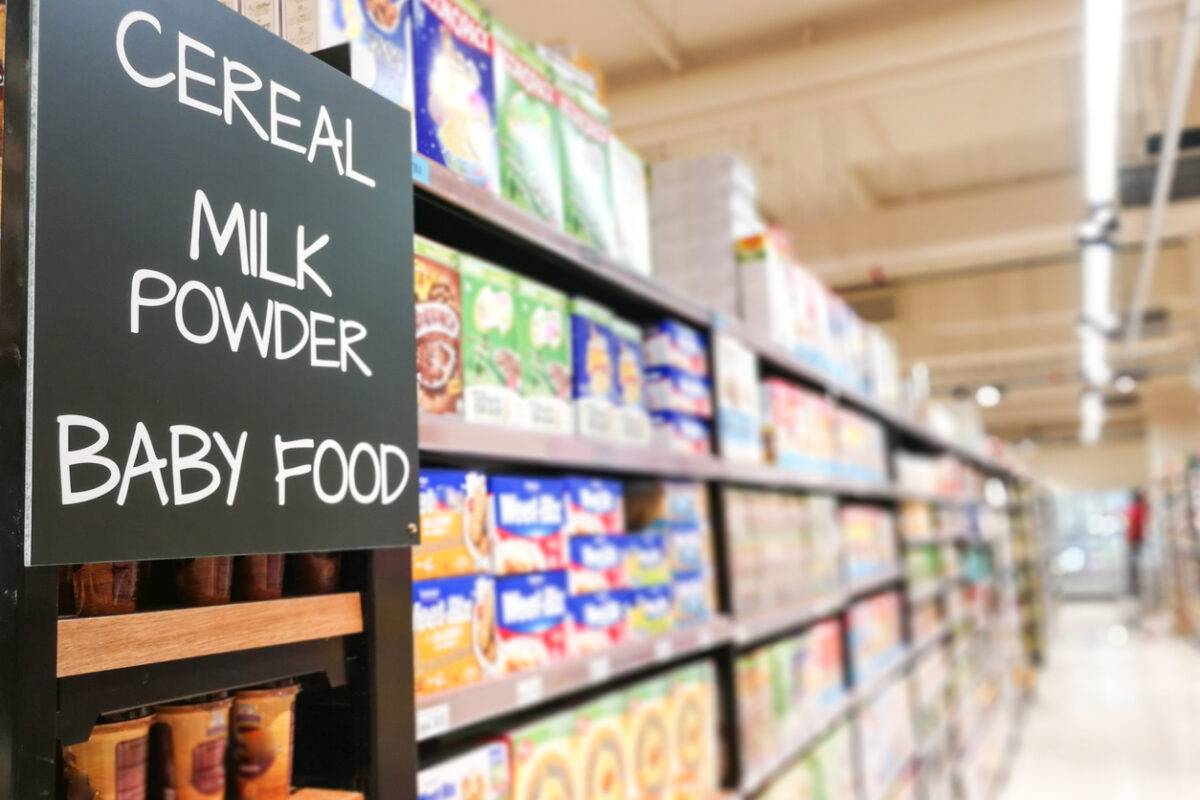 Close-up of a grocery store aisle with shelves of cereal and baby food, and a sign reading “Cereal, Milk Powder, Baby Food,” representing WIC-eligible items.