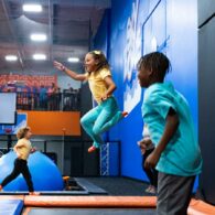 Kids jumping on trampolines at an indoor Sky Zone park with padded walls and bright play features.