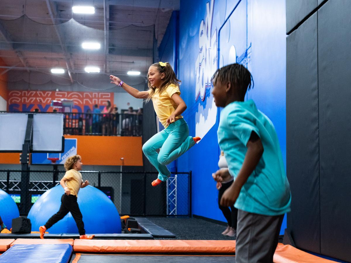 Kids jumping on trampolines at an indoor Sky Zone park with padded walls and bright play features.