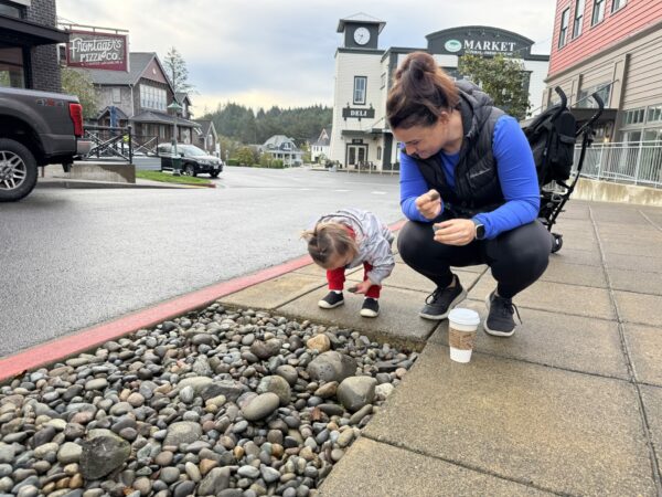 Parent and toddler collecting rocks along a Seabrook, Washington pathway on a cloudy fall day, bundled in jackets and rain boots.